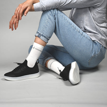 Person wearing black sneakers with white soles and white socks on a gray background