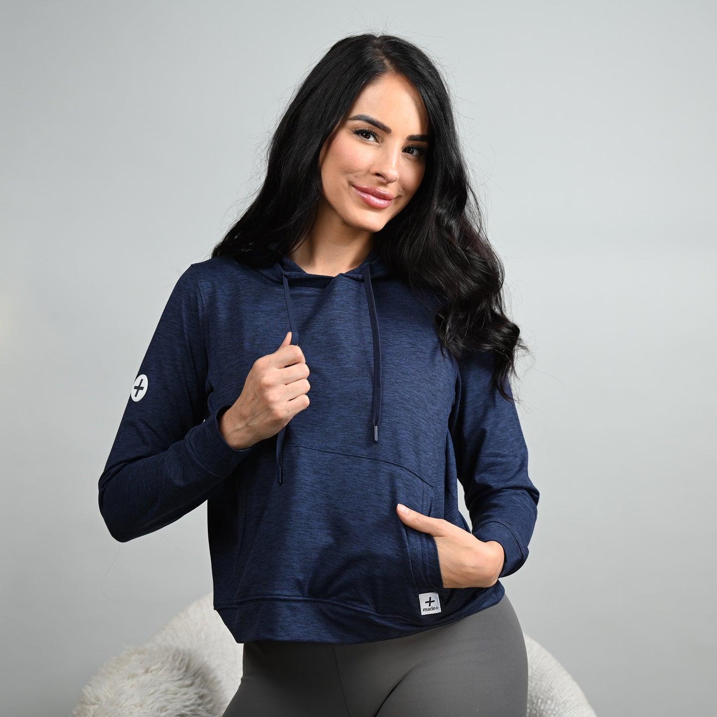 Woman wearing a navy blue hoodie with a logo on a gray background